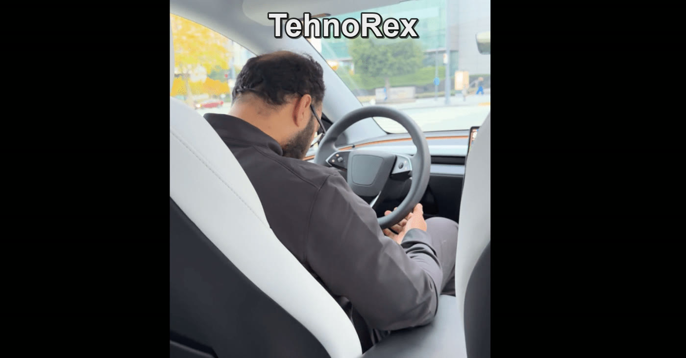 Водитель Tesla смотрит в телефон, руки у руля, город за стеклом