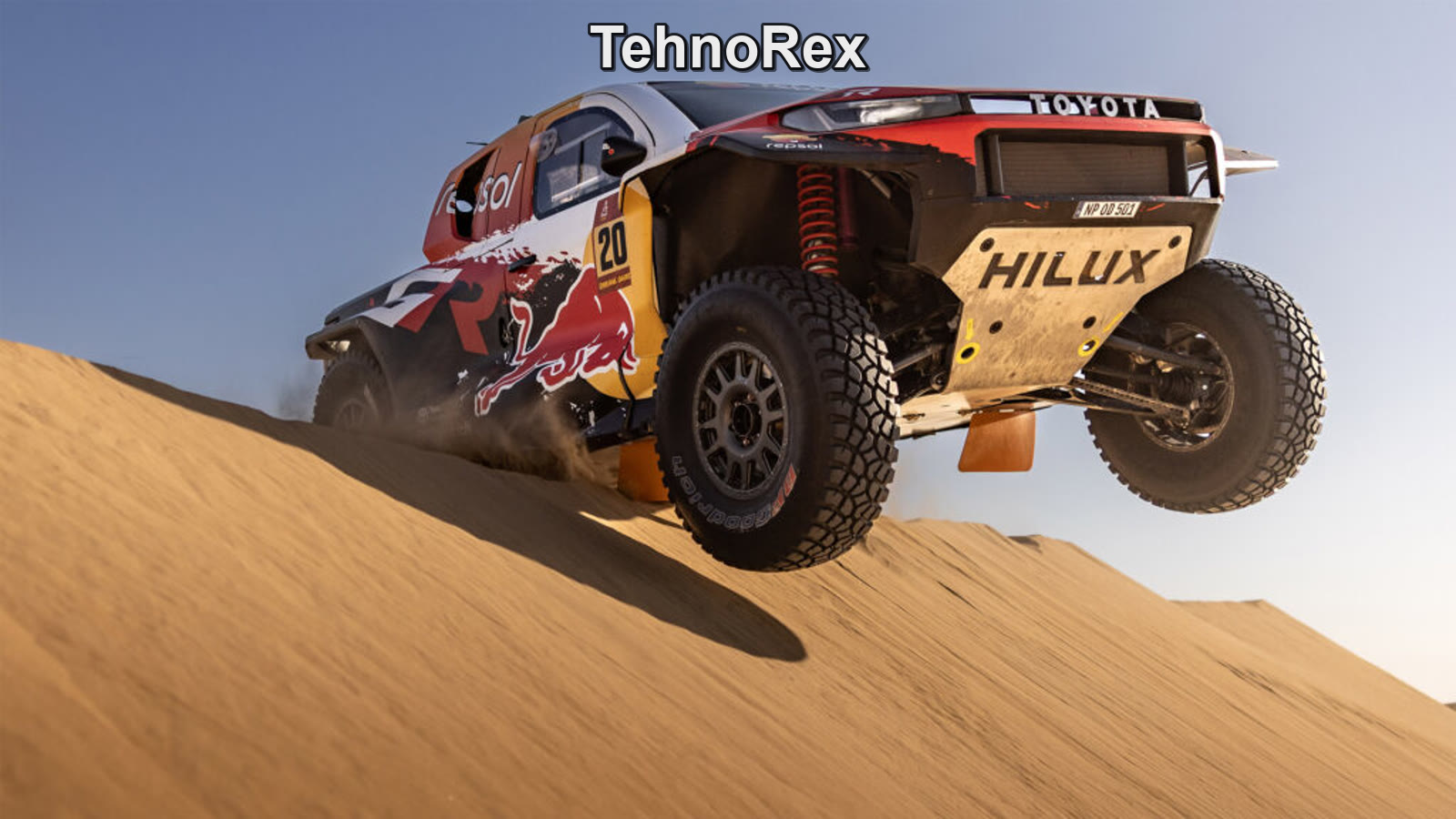 Toyota Hilux в красно-жёлтой ливрее прыгает с дюны на ралли-рейде